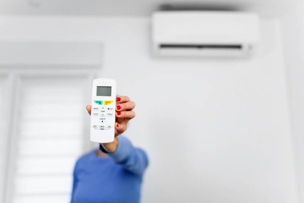 Woman holding a remote of a modern airconditioner unit at home. - Photo, Image