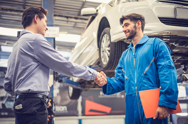 Mechanic holding clipboard shaking hands with car owner in the workshop garage. Car auto services concepts - Photo, Image