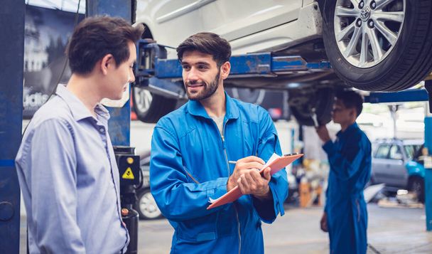 Mechanic holding clipboard with car owner in the workshop garage. Car auto services concepts - Photo, Image