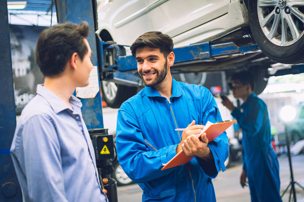 Mechanic holding clipboard with car owner in the workshop garage. Car auto services concepts - Φωτογραφία, εικόνα
