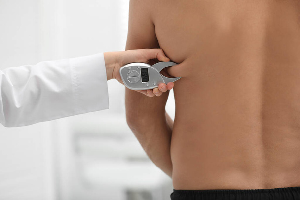 Nutritionist measuring man's body fat layer with digital caliper on blurred background, closeup - Photo, image
