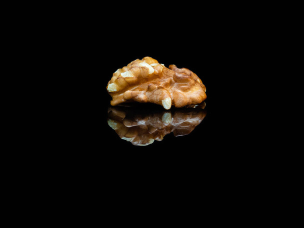 Half nut projects its reflection on a shiny black background - Foto, afbeelding