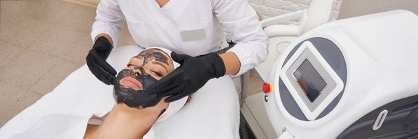 Косметолог наносить чорну маску на обличчя красивої жінки для вуглецевої шкірки
 - Фото, зображення
