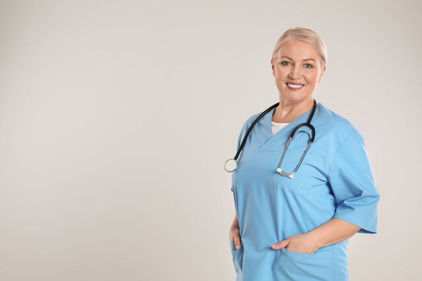 Portrait of mature doctor with stethoscope on light grey background. Space for text - Photo, image