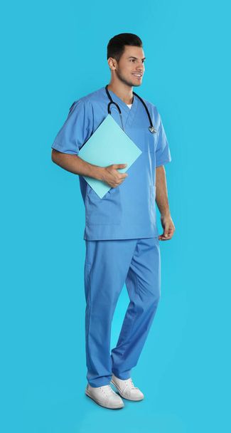 Handsome doctor with clipboard on blue background - 写真・画像