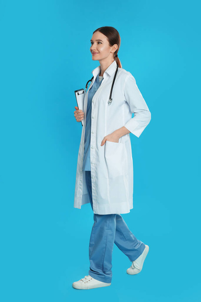 Doctor with clipboard and stethoscope walking on blue background - Фото, зображення