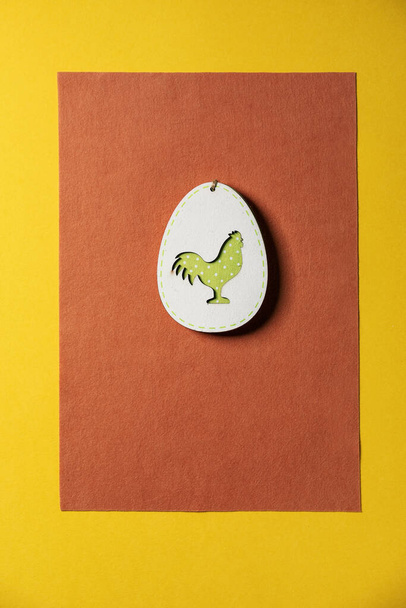 Minimal Easter greeting card with wooden decoration egg with chicken inside on bright felt orange yellow background. Flat lay, copy space. - Zdjęcie, obraz