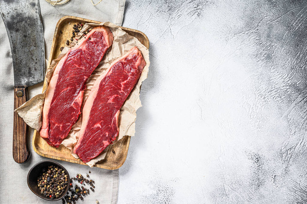Rohe Roastbeef-Steaks auf einem hölzernen Tablett mit einem Fleischspalter. Marmorrind. Grauer Hintergrund. Ansicht von oben. Kopierraum. - Foto, Bild