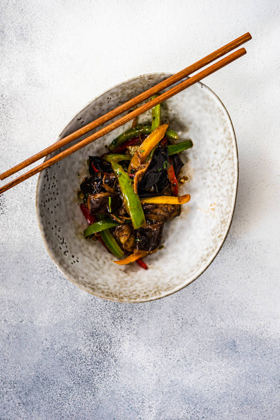 piatto asiatico vegetale cucinato in wok derved in ciotola di ceramica e bacchette di legno su sfondo di pietra con spazio copia
 - Foto, immagini