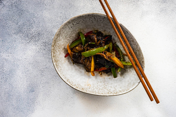 Zeleninové asijské jídlo vařené ve wok derved v keramické míse a dřevěné hůlky na kamenném pozadí s kopírovacím prostorem - Fotografie, Obrázek