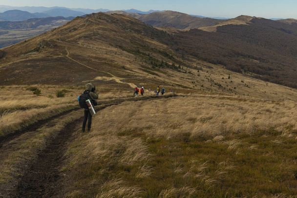 grupo de personas caminando en la meseta de las tierras altas a lo largo de la ruta turística sendero solitario tierra en la cresta de la montaña crepúsculo iluminación otoño gris temporada
 - Foto, Imagen