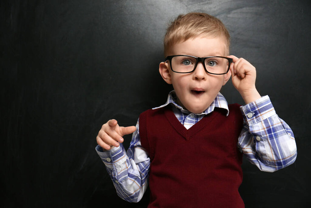 Cute little child wearing glasses near chalkboard. First time at school - Foto, Imagem
