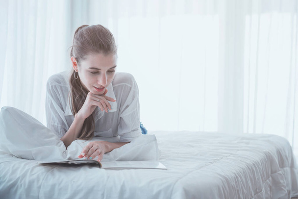 Jeune femme lisant sur le livre et s'allongeant sur le lit à la maison
. - Photo, image