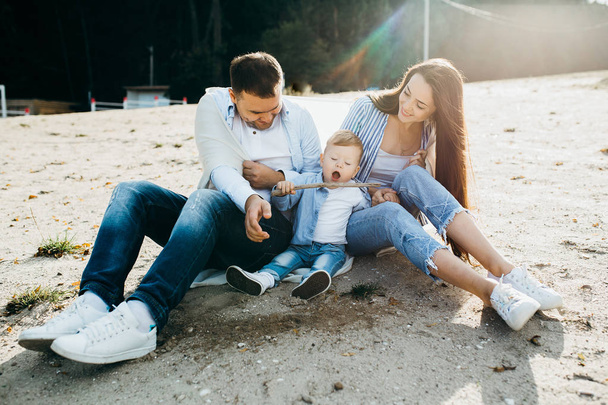 Schöne glückliche Familie, die an der Küste sitzt, während sie an einem Frühlingstag in der Nähe des Sees spaziert. - Foto, Bild