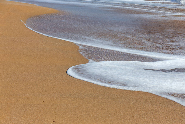 Een zachte zeegolf rolt over het zand van het strand. Zeegezicht golven aan de kust - Foto, afbeelding