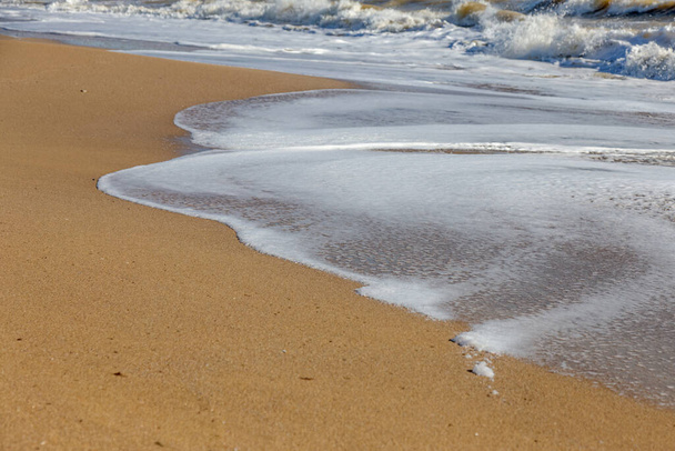 Ένα απαλό κύμα κυλάει στην άμμο της παραλίας. Θαλασσινά κύματα στην ακτή - Φωτογραφία, εικόνα