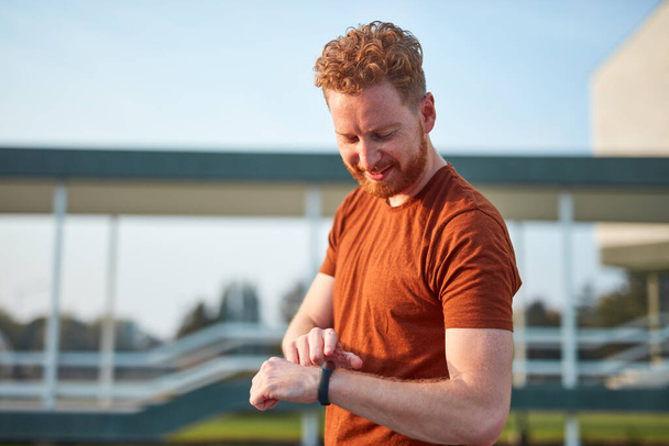 Young man using hand watch during exercising / stretching in urban park. - Fotoğraf, Görsel