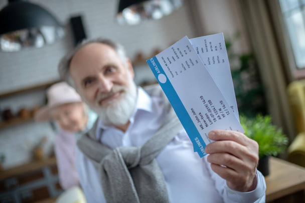 Smiling elderly man holding two boarding passes - Foto, afbeelding