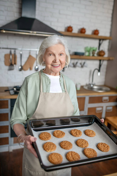 Smiling elderly woman holding just baked cookies - Foto, afbeelding