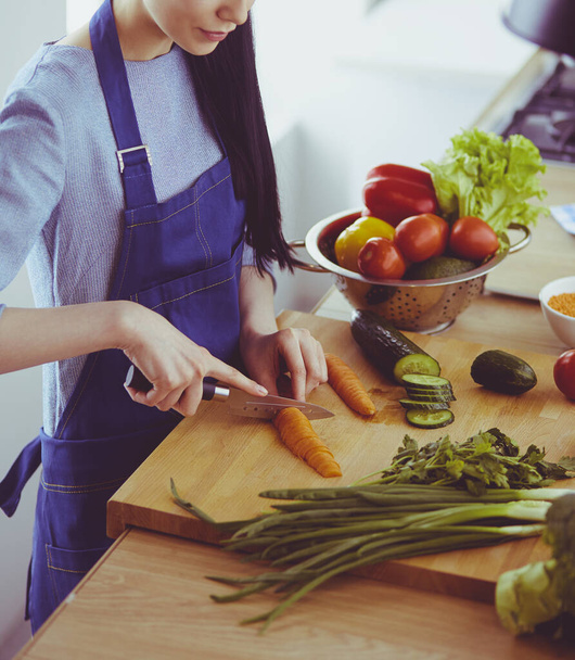 Jeune femme coupant des légumes dans la cuisine à la maison - Photo, image