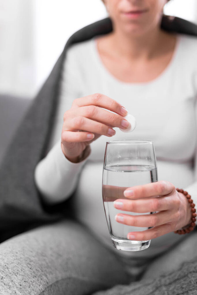 Pregnant woman taking vitamin tablet in a glass of water. - 写真・画像