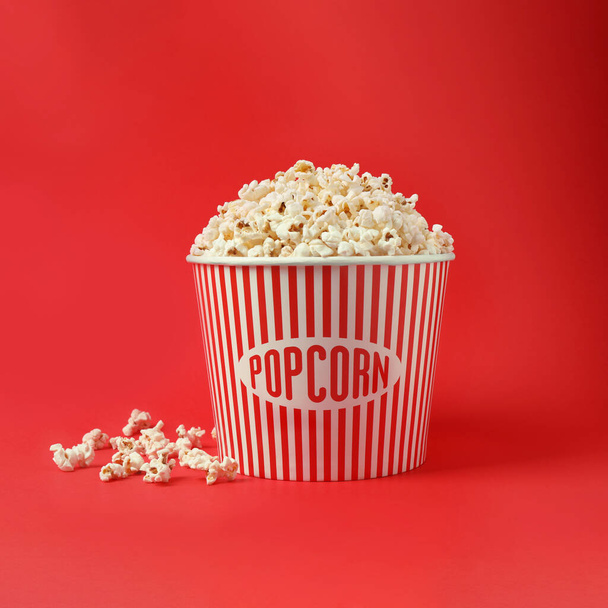 Delicious popcorn in paper bucket on red background - Foto, afbeelding