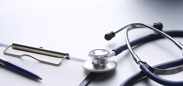 Medical stethoscope with clipboard on wooden desk - Fotó, kép