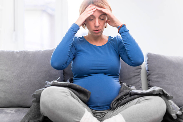 Pregnant tired exhausted woman with stomach and head issues at home on a couch, being sick. - Foto, Imagen