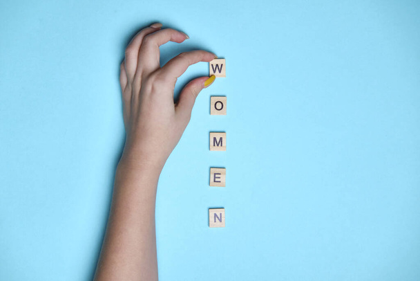 Top view women spelled in wooden blocks on blue background. Woman hand. Love, 8 march background. Gift, greeting, compliment concept. Copy space. place for text - Fotografie, Obrázek