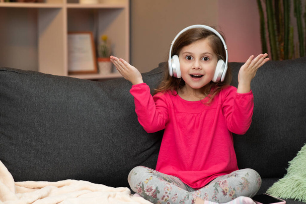 Little Girl Listens To Music On Wireless Headphones. Funny Little Girl Dancing, Singing And Moving To Rhythm. Kid Wearing Headphones. - Foto, afbeelding
