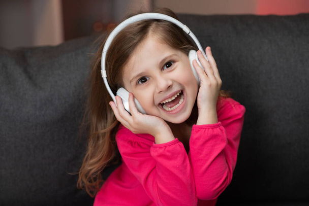 Beautiful Cute Happy Little Girl Listens To Music On Wireless Headphones. Funny Little Girl Dancing, Singing And Moving To Rhythm. Kid Wearing Headphones. - Фото, зображення