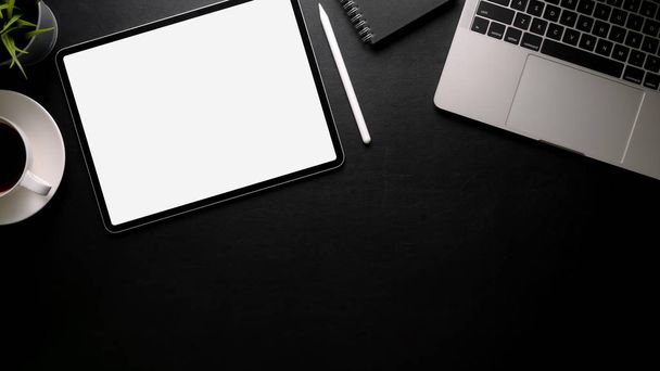 Снимок темного современного рабочего пространства с чистым экраном планшета, ноутбука, чашки кофе и копировального места на черном столе
  - Фото, изображение