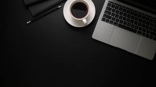 Toma aérea de espacio de trabajo moderno oscuro con computadora portátil, papelería, taza de café y espacio de copia en la mesa negra
  - Foto, Imagen