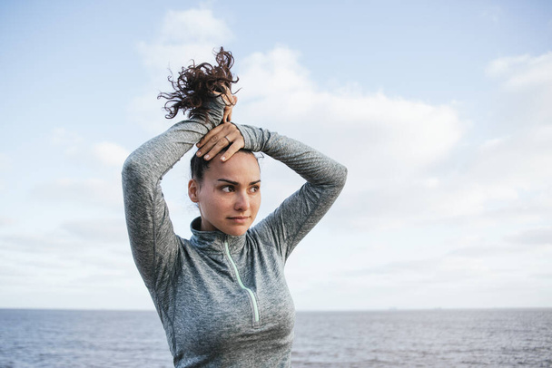 mladá latinská dívka vázání vlasy, s větrem, a sportovní oblečení, s mořem na pozadí - Fotografie, Obrázek