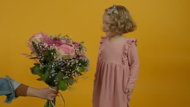 Fröhlich lockiges Kind, das Blumen betrachtet und auf gelbem Hintergrund springt - Filmmaterial, Video