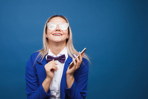Cute and funny businesswoman in a stylish blue jacket and bow tie uses a smartphone. - Foto, afbeelding