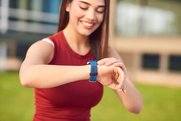 Jeune femme faisant de l'exercice / s'étirant dans un parc urbain et regardant la montre-bracelet pour vérifier l'heure
. - Photo, image