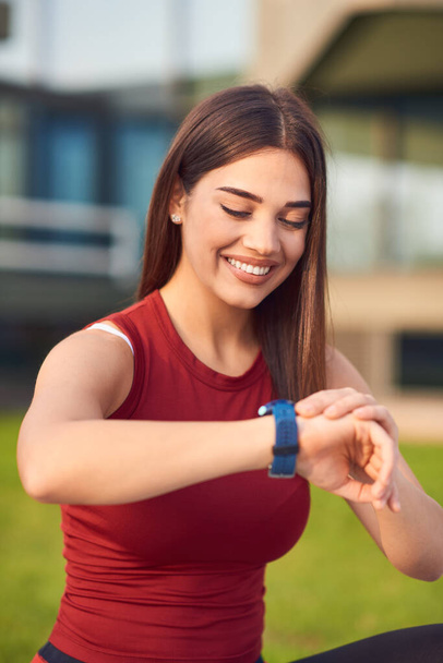 Mujer joven haciendo ejercicio / estiramiento en el parque urbano y mirando el reloj de pulsera para comprobar la hora
. - Foto, imagen