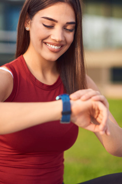 Young woman exercising / stretching in urban park and looking at the wristwatch to check time. - Photo, Image