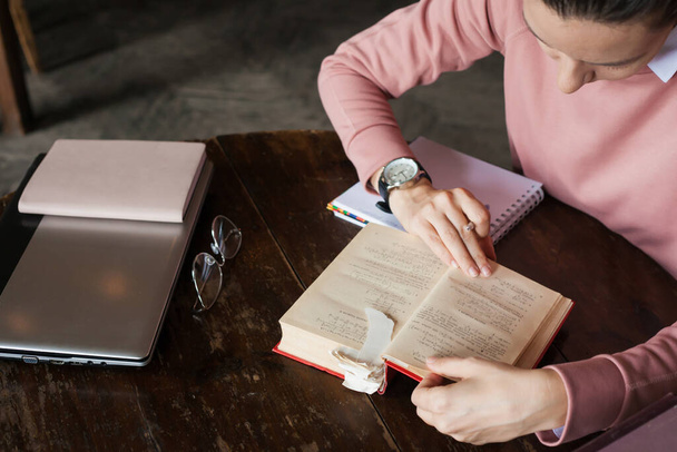 Dívka v růžovém svetru listuje v husté knize s mnoha záložkami, dělá si poznámky, požyje pero, ruce na knihu. - Fotografie, Obrázek