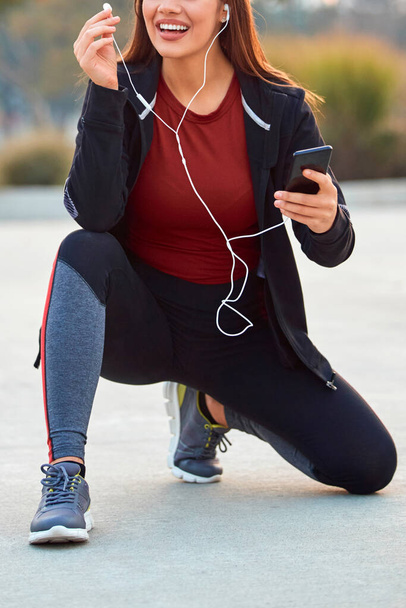 ジョギング/運動中に一時停止する携帯電話を持つ現代の若い女性. - 写真・画像