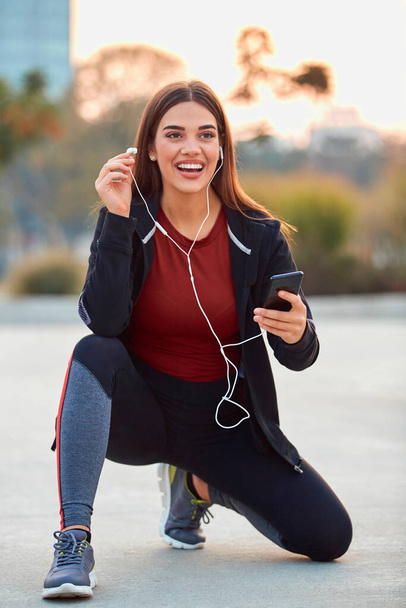 Moderne jonge vrouw met mobiele telefoon maken pauze tijdens joggen / lichaamsbeweging. - Foto, afbeelding
