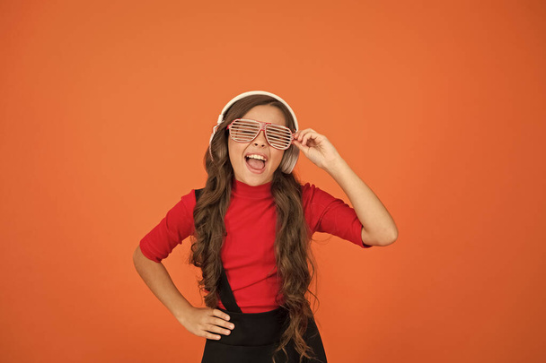 using wireless headset for DJ disco. small happy girl listen music in headphones. funny child in party glasses. time having fun. modern kid enjoy music. feeling stylish and confident. school radio dj - Foto, afbeelding