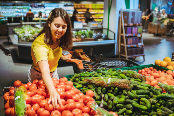 vrouw kiezen rode tomaten uit winkel plank kruidenier winkelen concept - Foto, afbeelding
