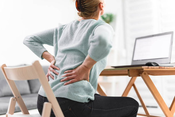 Femme travaillant sur un ordinateur portable et ayant mal au dos, à la hanche, à la colonne vertébrale
. - Photo, image