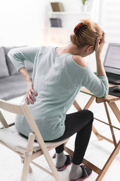 Woman working on a laptop and having headache and back, hip, spine pain. - Photo, Image