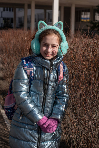 Beautiful young cute woman in blue coat is posing. Fashion trendy style clothes. Beautiful girl outdoors in winter in a blue jacket. 9 years old. Girl with a backpack pulled from school. Girl rejoices - Photo, Image