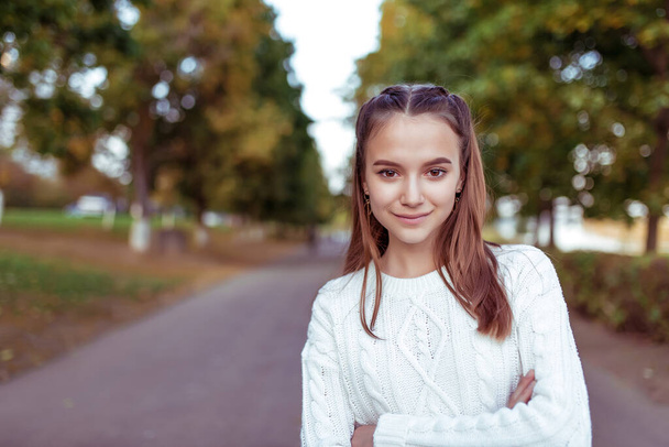 Portrait of a teenage girl of 12 years old, in summer in park, casual clothes, white knitted sweater, free space for copy text. Weekend break. Emotions of happiness are smiles and positive. - 写真・画像
