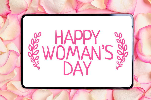 Tabletka na tle płatków róż z abstrakcyjnym napisem - Happy Women 's Day z gałązkami po bokach. Widok z góry. - Zdjęcie, obraz