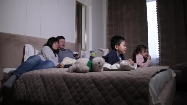 Happy asian family with kids watching TV on bed - Video